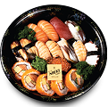 Naeki's large, black, round platter of assorted sushi. The platter is filled with rows of various nigiri sushi, including salmon, tuna, eel, white fish, and octopus. In the bottom section, there is a row of maki rolls with salmon and what appears to be egg. A small, yellow square card with the restaurant's logo, "MAKI," is placed in the center of the platter.