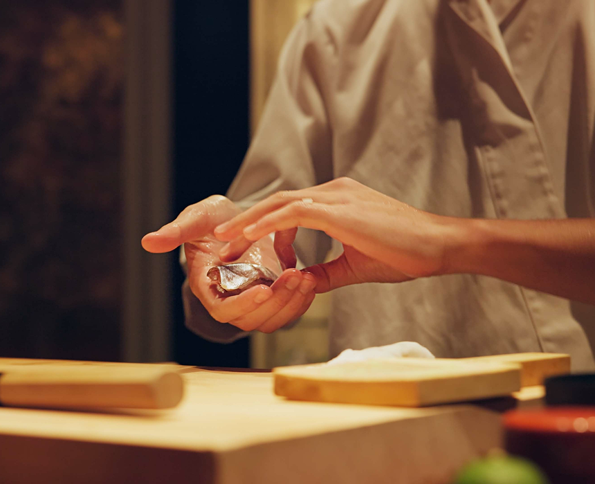 Sushi chef's hands preparing nigiri with silver-skinned fish and rice.